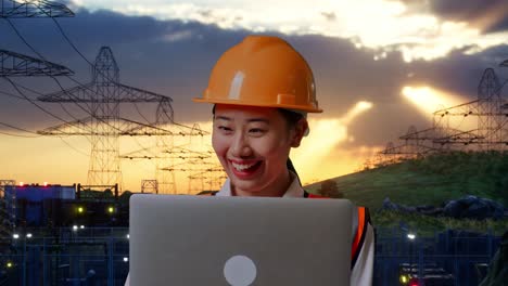 primer plano de una ingeniera asiática con casco de seguridad trabajando en una computadora portátil mientras está de pie cerca de una torre de alto voltaje