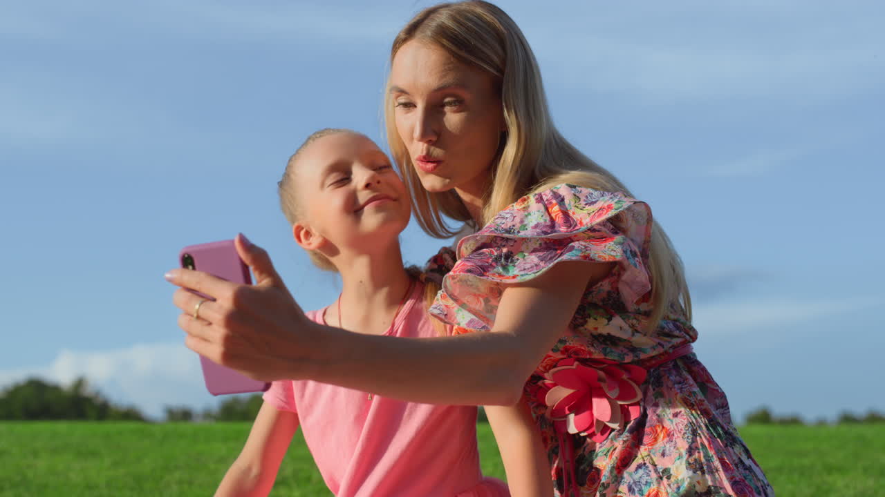 Mor och dotter som har videosamtal på mobiltelefon på grön äng