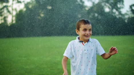 Boy-standing-in-green-meadow.-Child-getting-wet-under-water-sprinkler-in-field