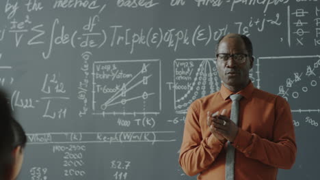 african american professor lecturing in classroom with blackboard of equations