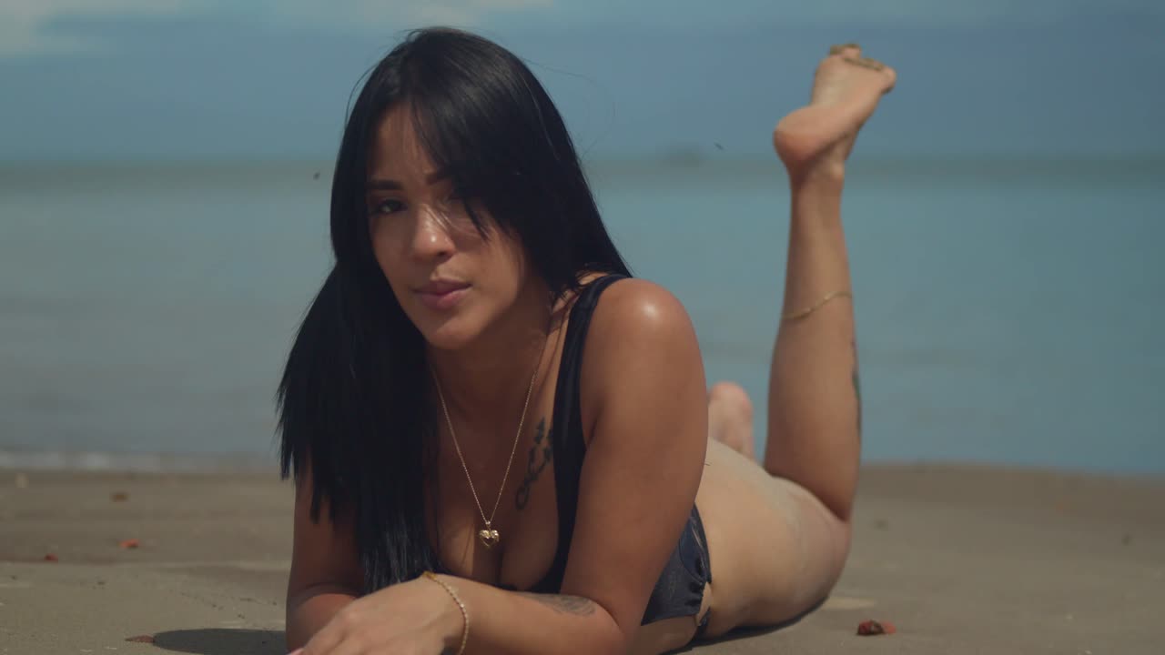 Embracing the sun's warmth on a sunny day, a Hispanic girl with long natural hair lay in the sand on tropical Caribbean beach in a bikini
