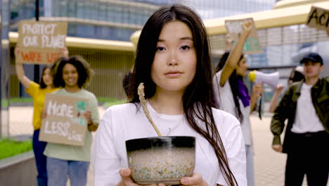 worried woman holding dead plant while her colleagues protest behind her