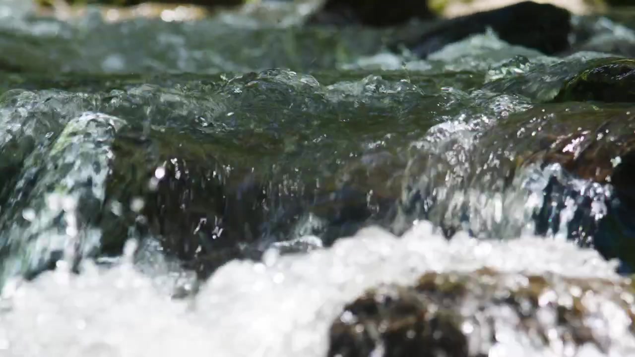Klar fjellbekk renner over glatte steiner. Vannet spruter og kruser med naturlig energi. Sollys reflekteres fra våte overflater, og fremhever bevegelse. Ideell for natur, reise.