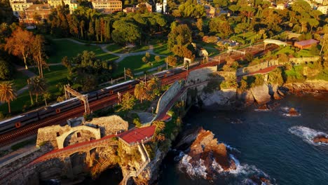 golden hour drone shot of genoa's coastline, showing lush parks, train tracks, and the sea