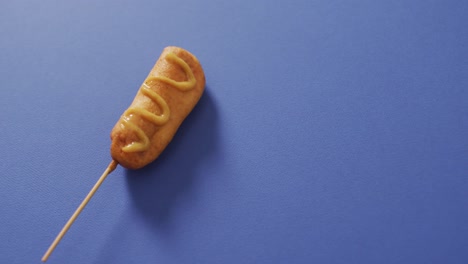 video of corn dog with mustard on a blue surface