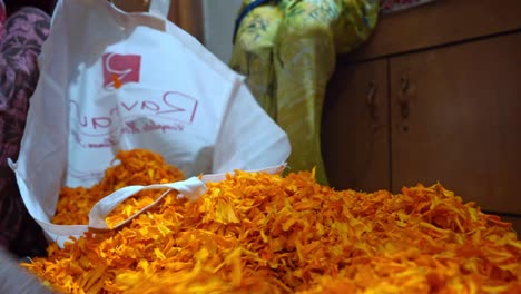 la mano de la mujer recoge un puñado de pétalos de flores de caléndula y los pone en una ecobolsa blanca en agra, india - toma de primer plano