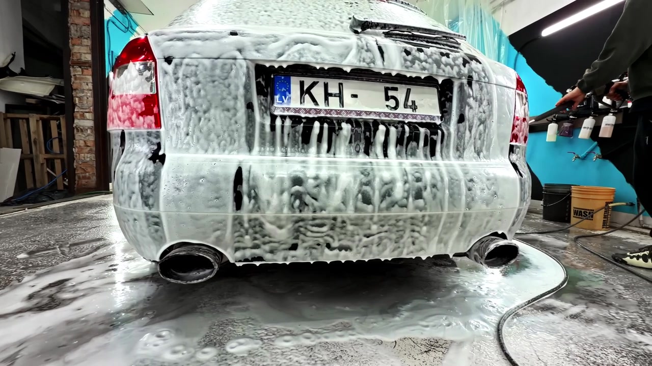 Parte posteriore di un'auto nera sottoposta a un lavaggio auto dettagliato con sapone schiumogeno presso un centro di detailing auto. Carrellata.