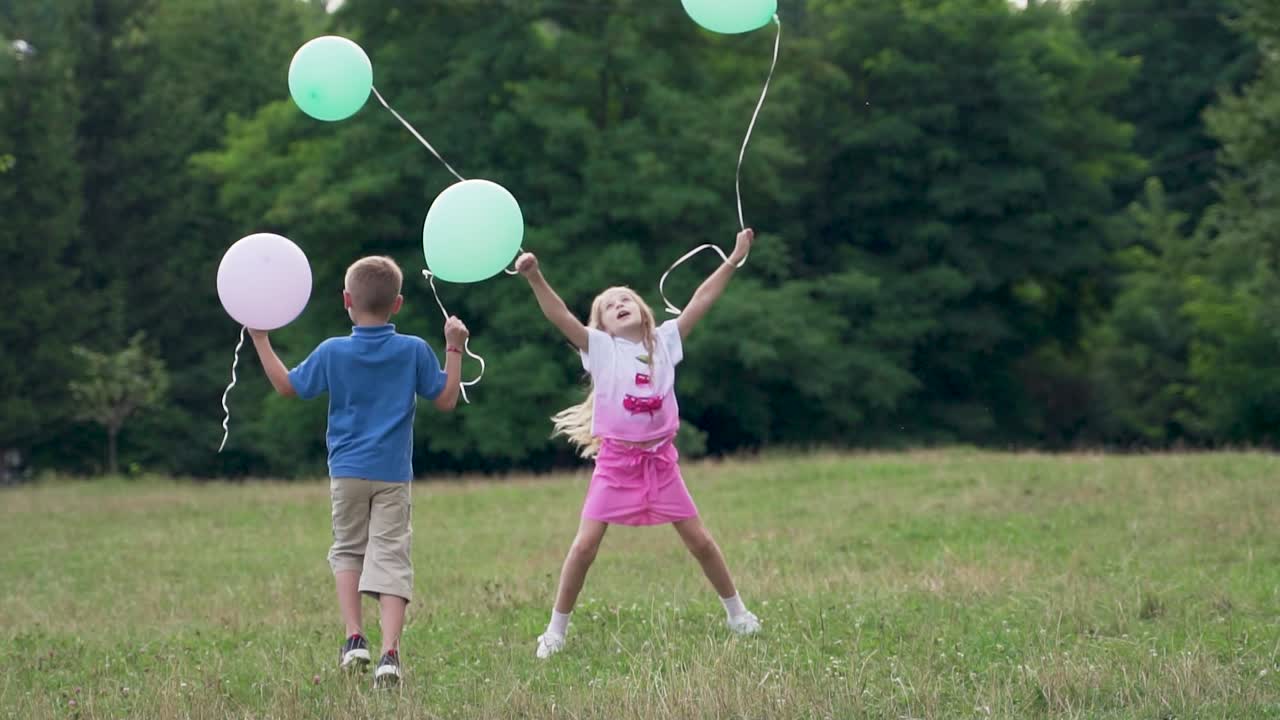 Happy boy and girl with balloons run in the park on the grass. Children's holiday birthday in nature in summer