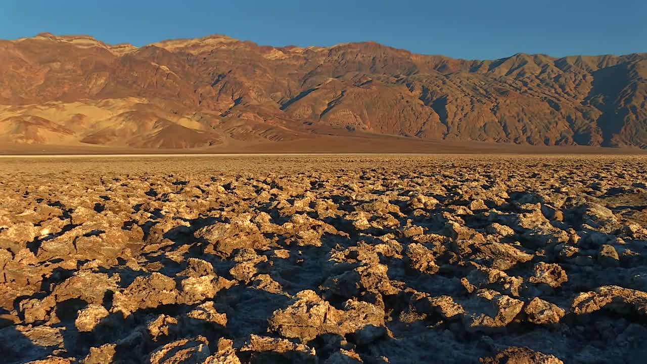 Salt and rock formations in arid desert foreground. Tilt up reveals distant mountain peaks in Death Valley National Park, California, USA