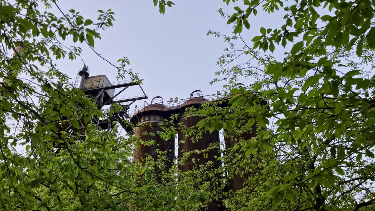 Silos in a metal framework in evening mood protrude between nature trees and leaves landscape park, duisburg, germany