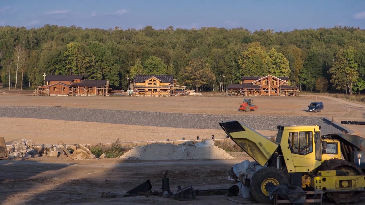 Landscape transform into urban area timelapse. View to wooden houses on construction site with bulldozer for new cottage village in a large field