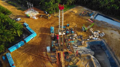 imágenes cinematográficas de drones de 4k de la estructura del equipo de la plataforma de perforación en tierra para la exploración y explotación de petróleo en medio de la jungla rodeada de palmeras durante la puesta de sol y el alto precio del petróleo