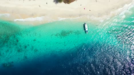 Tiefblaues-Meer-Und-Türkisfarbene-Lagune,-Die-Auf-Dem-Weißen-Sand-Eines-Exotischen-Strandes-Weht,-Verankertes-Boot,-Das-über-Felsigen-Meeresboden-Schwimmt-Und-Durch-Kristallklares-Wasser-Gesehen-Wird