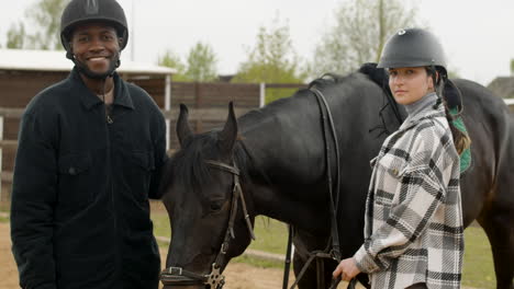 dos amigos acariciando el caballo negro y mirando la cámara al aire libre 1