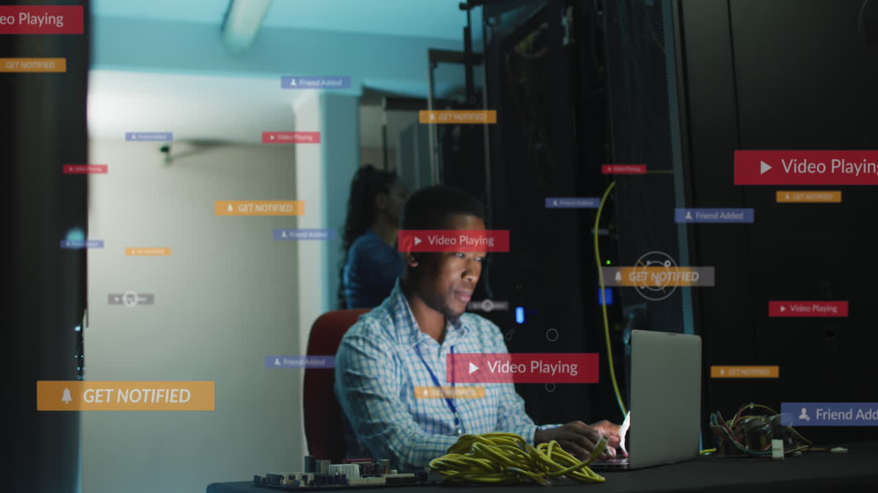 animación de iconos de redes sociales sobre un ingeniero afroamericano usando una computadora portátil en la sala del servidor