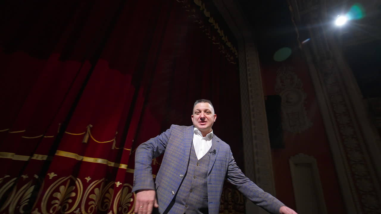 Actor man speaking and dancing on stage. Man in suit on stage in front of empty audience. Orbiting shot.