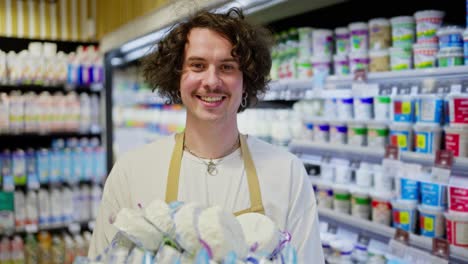 Portrait-of-a-happy-guy-holding-in-his-hands-a-box-of-cottage-cheese-and-other-dairy-products-in-a-department-in-a-supermarket