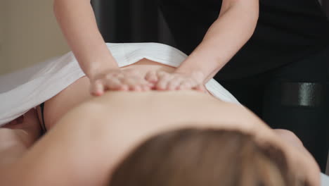 massage therapist rubbing cream on back of light skin woman lying on massage table, partially covered with white towel, capturing soothing spa therapy moment focused on relaxation and skincare