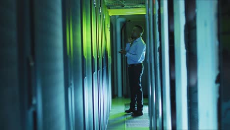 African-american-male-computer-technician-using-smartphone-working-in-business-server-room