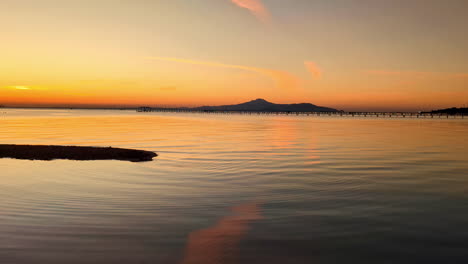 aerial sunset landscape above african beach coastline, volcano hills gradient, orange golden light blue vibrant skyline over reflected calm still sea water