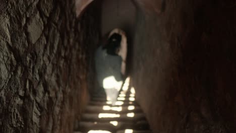 silhouetted figure walking up ancient stone steps in dimly lit tunnel, mystery and history combined, handheld shot