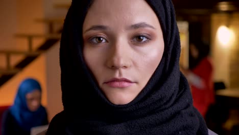 closeup portrait of young beautiful arabian businesswoman in black hijab turning to camera from the side and looking straight