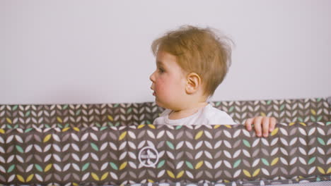 Front-View-Of-Baby-In-White-Bodysuit-Smiling-And-Playing-Hide-And-Seek-Inside-The-Baby-Playground