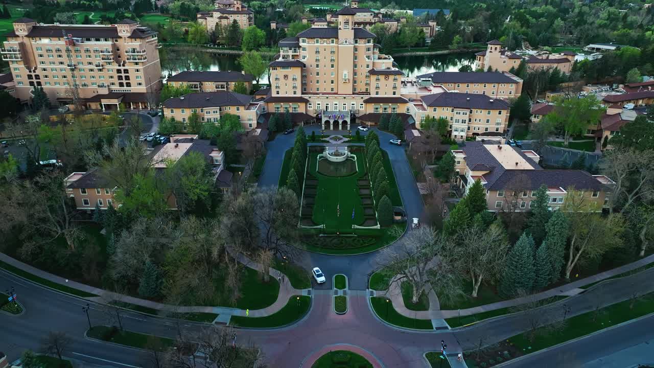 Broadmoor estate bordered by lake and trees, aerial approach under soft sunset glow