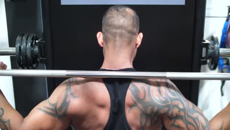 a muscular male bodybuilder lifting weights at the gym from the back