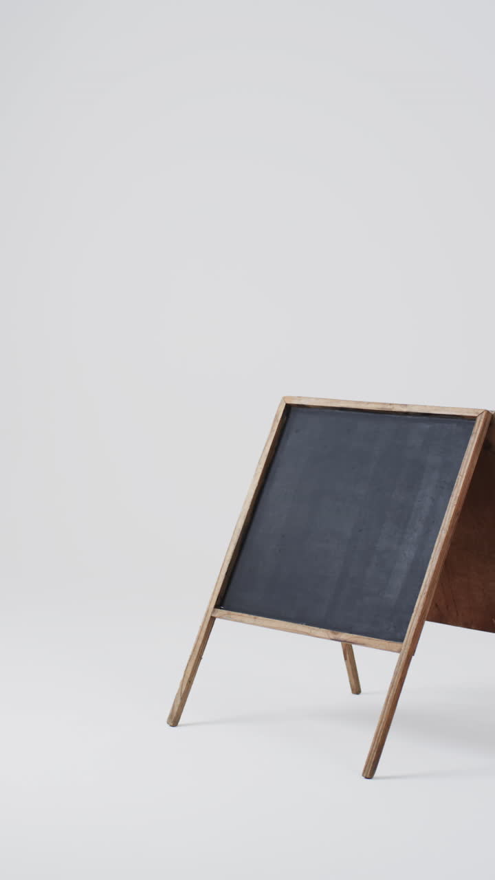 Vertical video of blackboard sign on wooden stand with copy space on white background