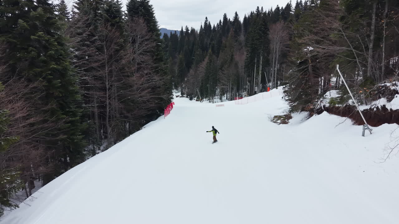 Uno snowboarder scende una pista da sci circondata da alberi in un paesaggio invernale durante le ore diurne in una regione montuosa.