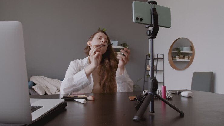 Giovane e carina vlogger che prova un mascara davanti alla fotocamera del suo smartphone.