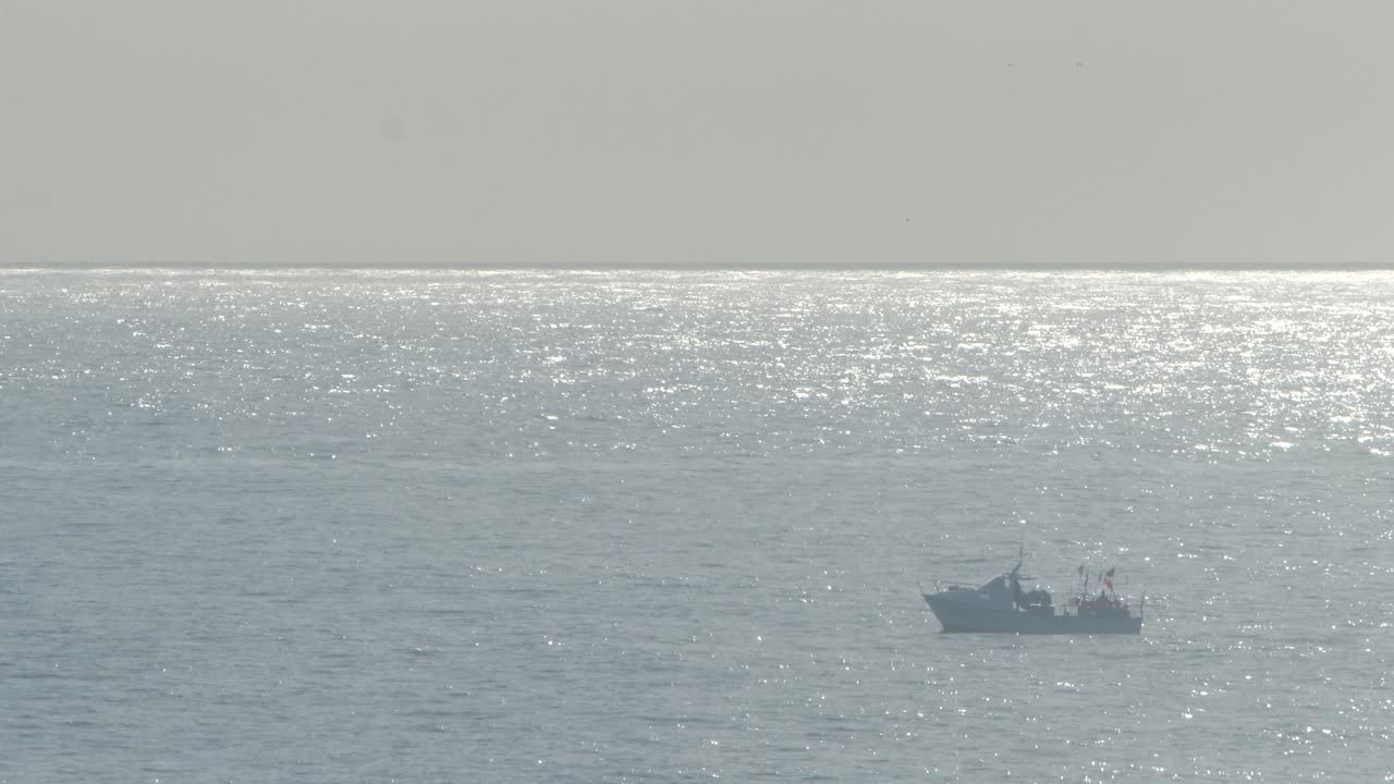 A fishing boat drifting on the ocean waves as a fisherman works on deck
