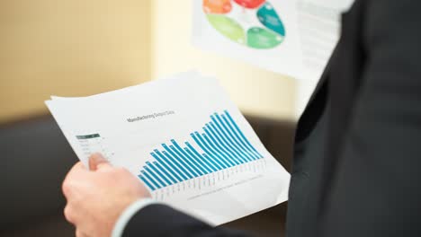 A business professional reviews printed data visualizations, including a colorful infographic with key insights and a bar chart showing performance metrics, while holding the documents hands close-up