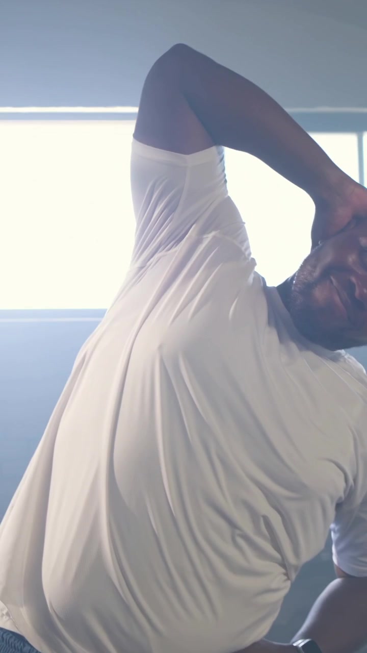 Vertical video: Starting warmup man in offwhite tee doing cross-arm stretch at gym, smartwatch