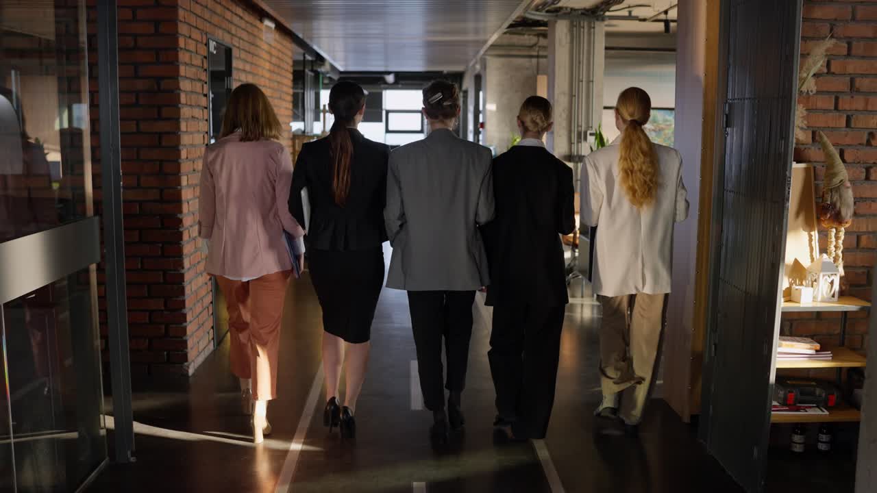 vista trasera de cinco mujeres de negocios confiadas caminando por el piso gris en una oficina moderna confiadas. cinco chicas confiadas en trajes de negocios caminan por la oficina