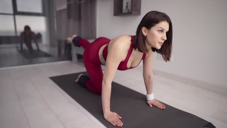 woman on mat practicing donkey kick exercise with ankle weight, raising one leg up