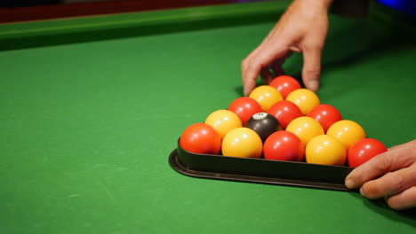 a man setting up the pool balls on a table in a triangle