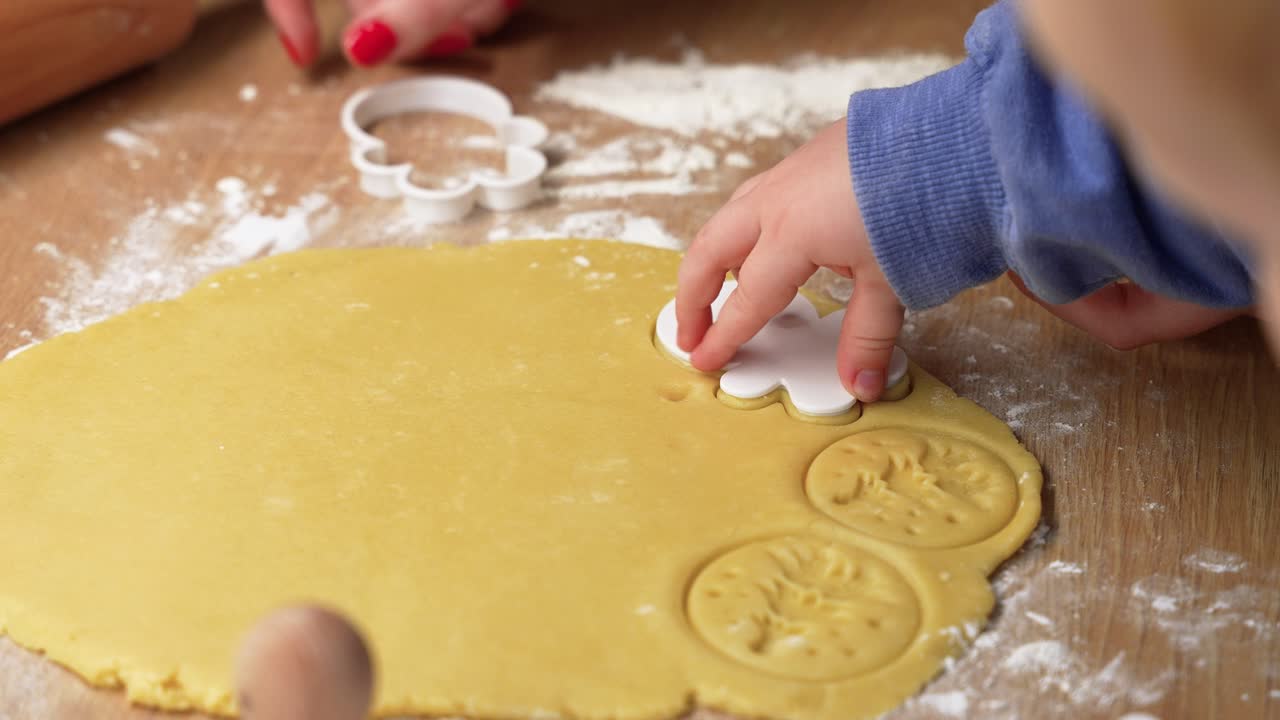 Detailed view of child's hands using dough cutters on cookie dough. Warm kitchen setting with soft lighting captures the joyful process of baking and creativity
