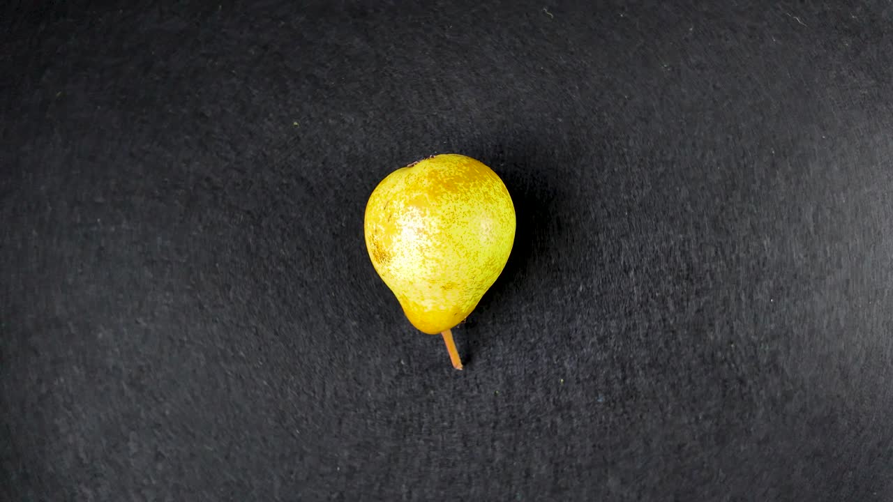 Fresh, ripe pear rotating slowly against a stark black background, creating a captivating visual