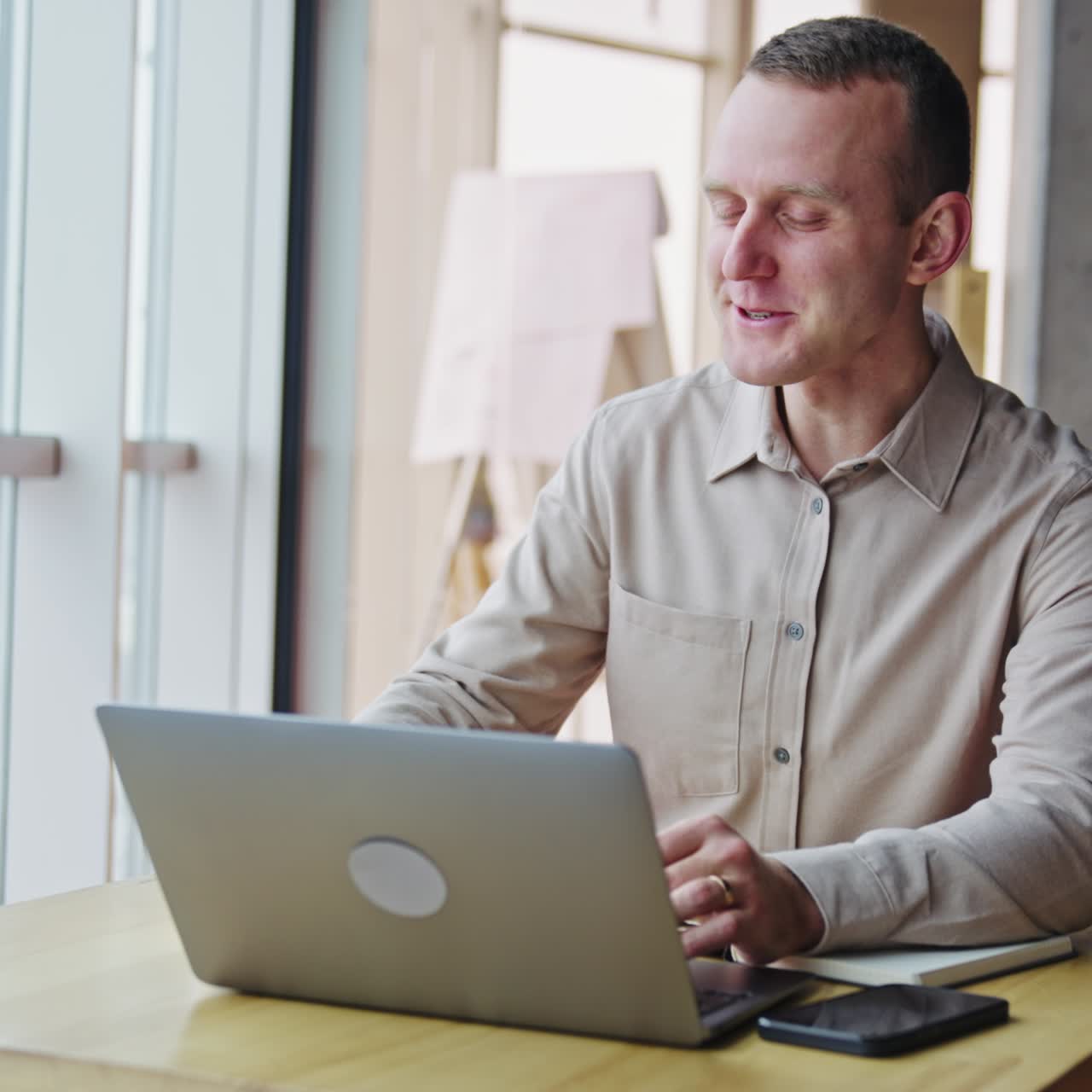 Resilient young man sitting at desk with laptop and having tea. Male having lunch break at workplace. Office backdrop