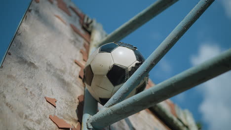 a close up of a worn and patched soccer ball wedged in a blue iron framework, with a bright sky in view