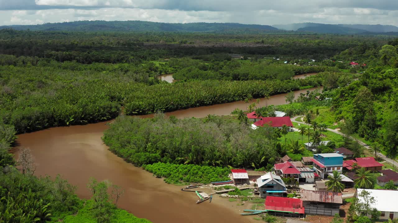 Flight above twisted murky river and small Indonesian fishing village