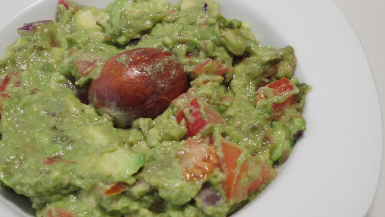 guacamole con semilla de aguacate en un tazón blanco, de la sartén a la izquierda en el plato central