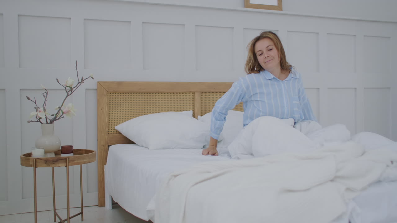 una mujer joven se despierta en la cama por la mañana sonriendo y estirándose. buen y alegre mañana.