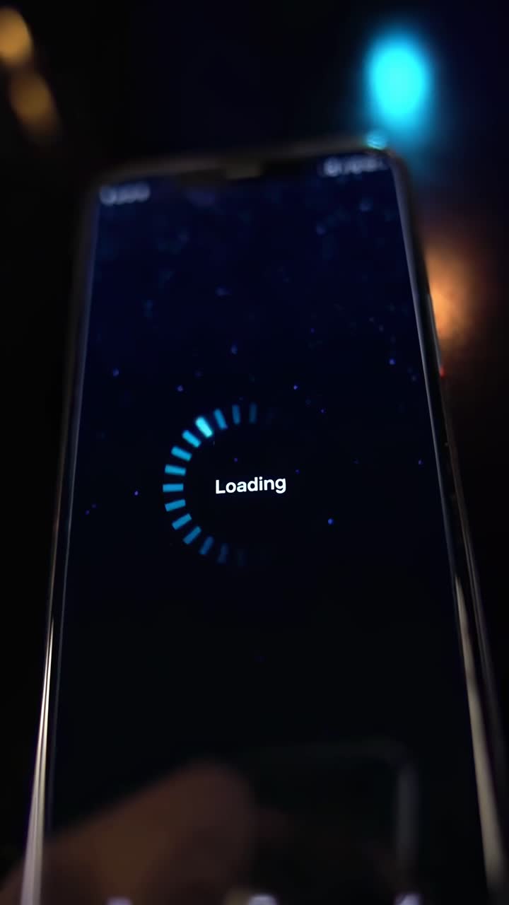Close-up angle of a smartphone screen showing a loading video, with a dark, moody style