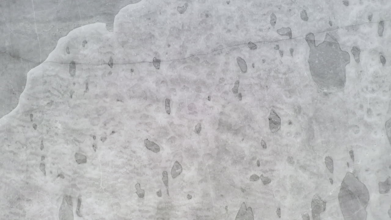 aéreo: toma vertical de un dron volando muy bajo y cerca de la superficie del lago congelado en un día nublado con bolsas visibles de hielo agrietado