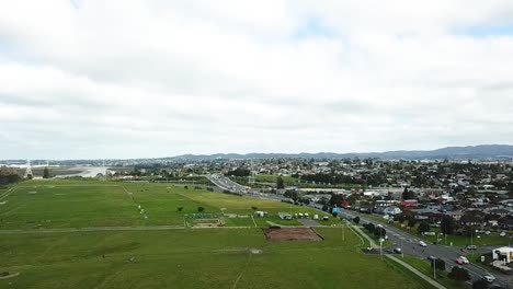 Luftaufnahme-Einer-Drohne-über-Einer-Großen-Farm-Auf-Der-Linken-Seite-Und-Starkem-Verkehr-Auf-Der-Rechten-Seite-In-Auckland,-Neuseeland