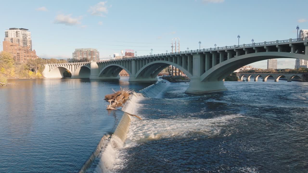 High aerial shot of the St. Anthony Falls Lock and Dam and the Third Avenue Bridge (Central Ave) over the Mississippi River, with the Minneapolis skyline in the background
