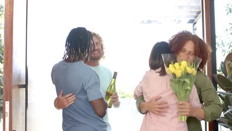 happy diverse couple embracing and greeting friends arriving at front door of home, slow motion